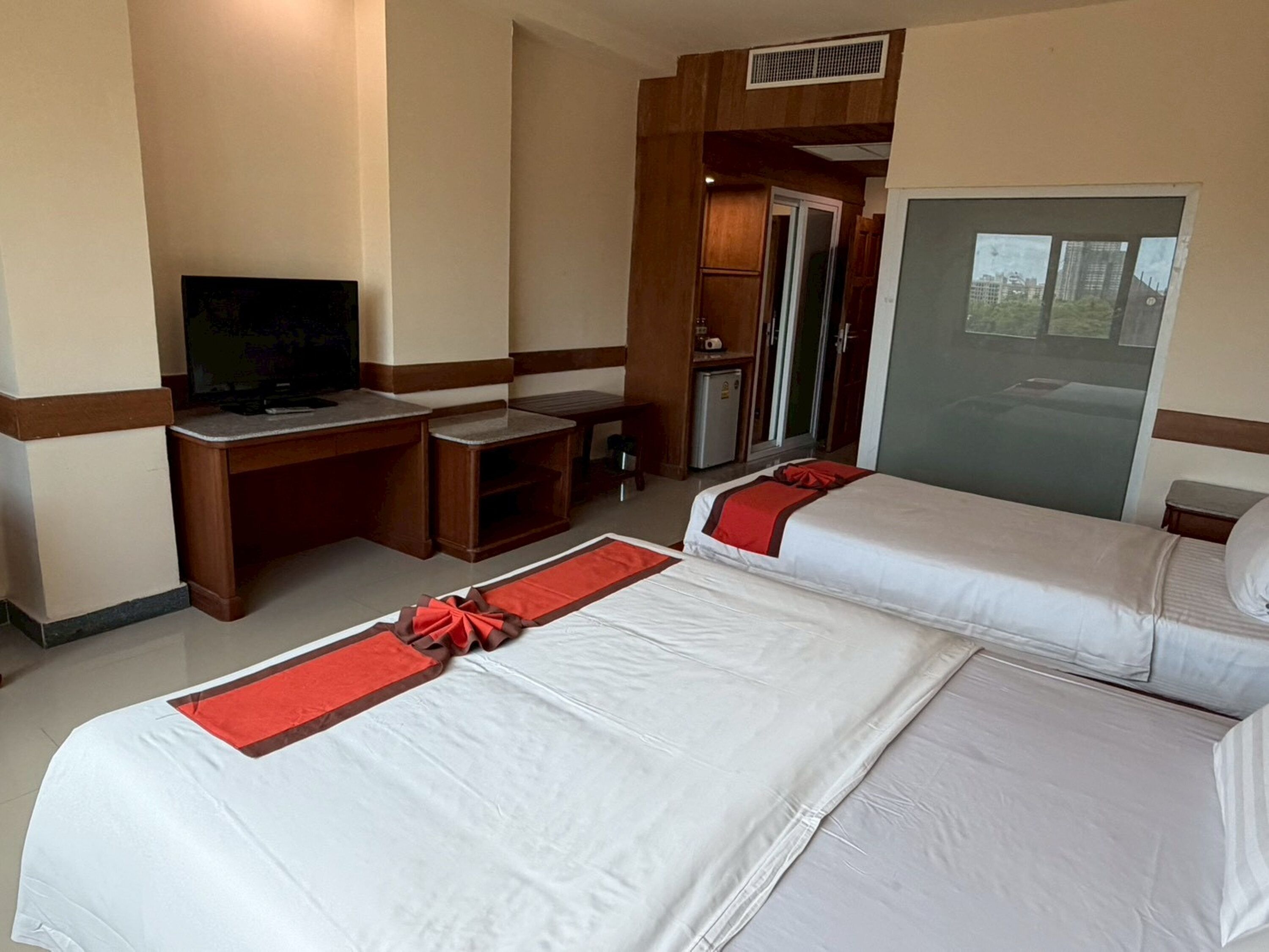 A hotel room with two beds, a desk, a television, and a view of the city.