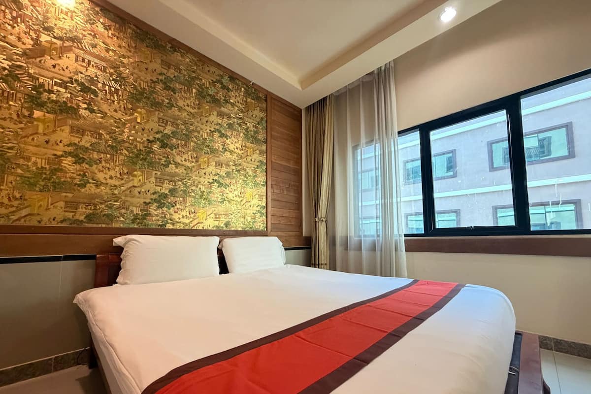 Une chambre d’hôtel avec un grand lit, une fresque murale, une fenêtre avec des rideaux et une vue sur les bâtiments environnants.