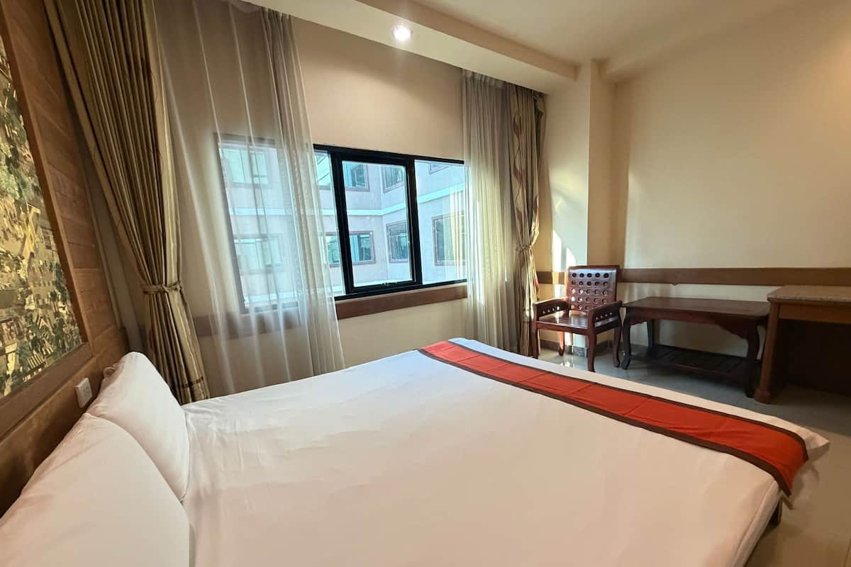 Une chambre d’hôtel avec un grand lit, un bureau, une chaise et une fenêtre avec des rideaux.