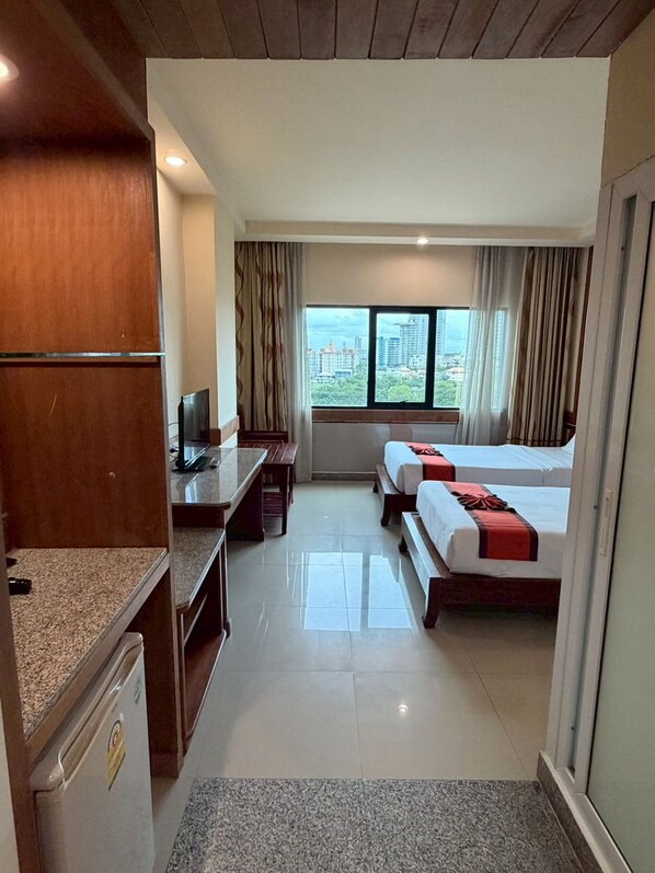 A hotel room with a bed, a desk, a television, and a window with a city view.