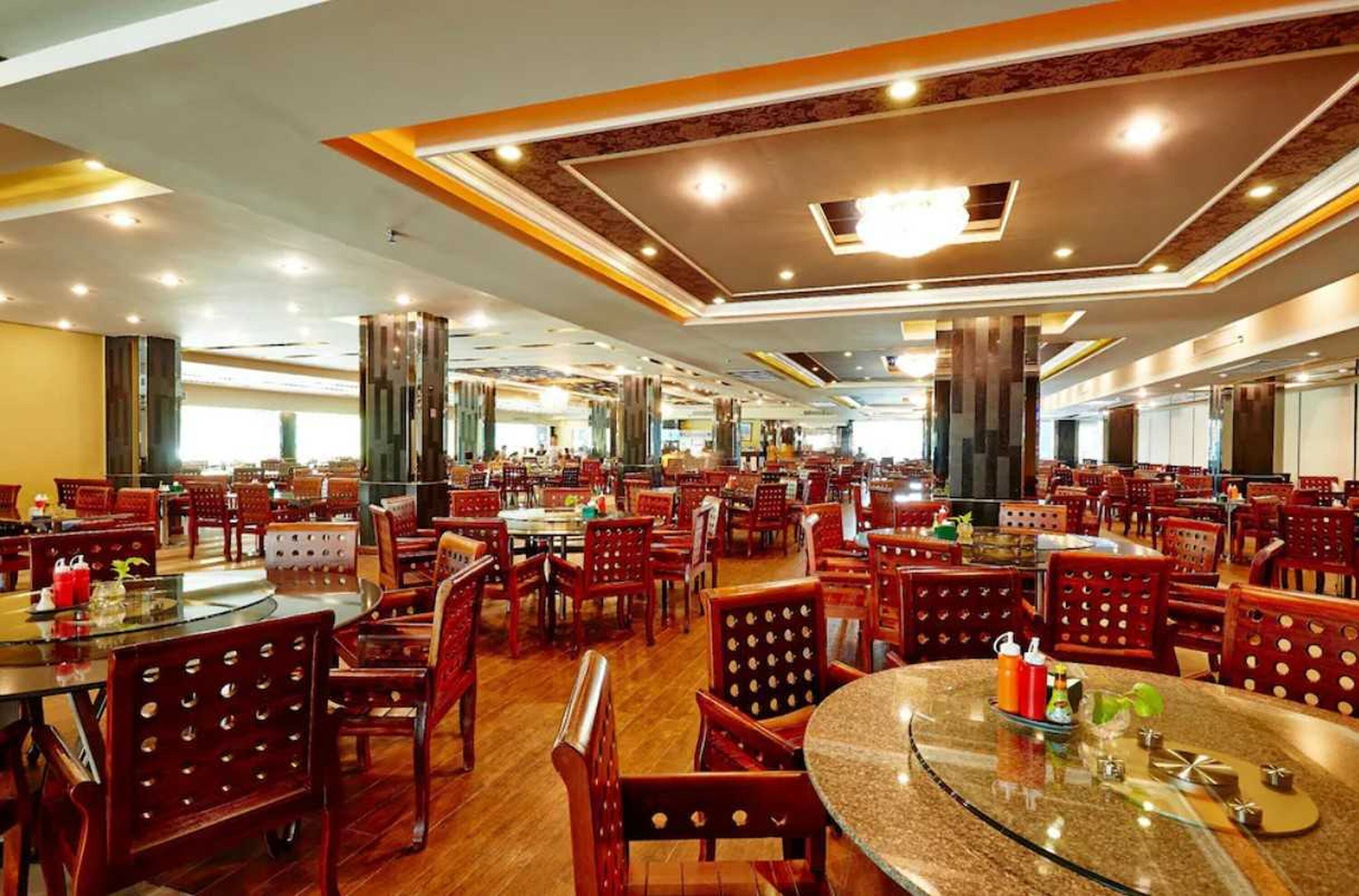 A spacious restaurant with multiple dining tables and chairs, high ceilings with recessed lighting, and a modern interior design.