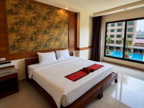 A hotel room with a large bed, a view of a swimming pool, and a cityscape through the window. - Sunday Grand Jomtien Pattaya (Pattaya)