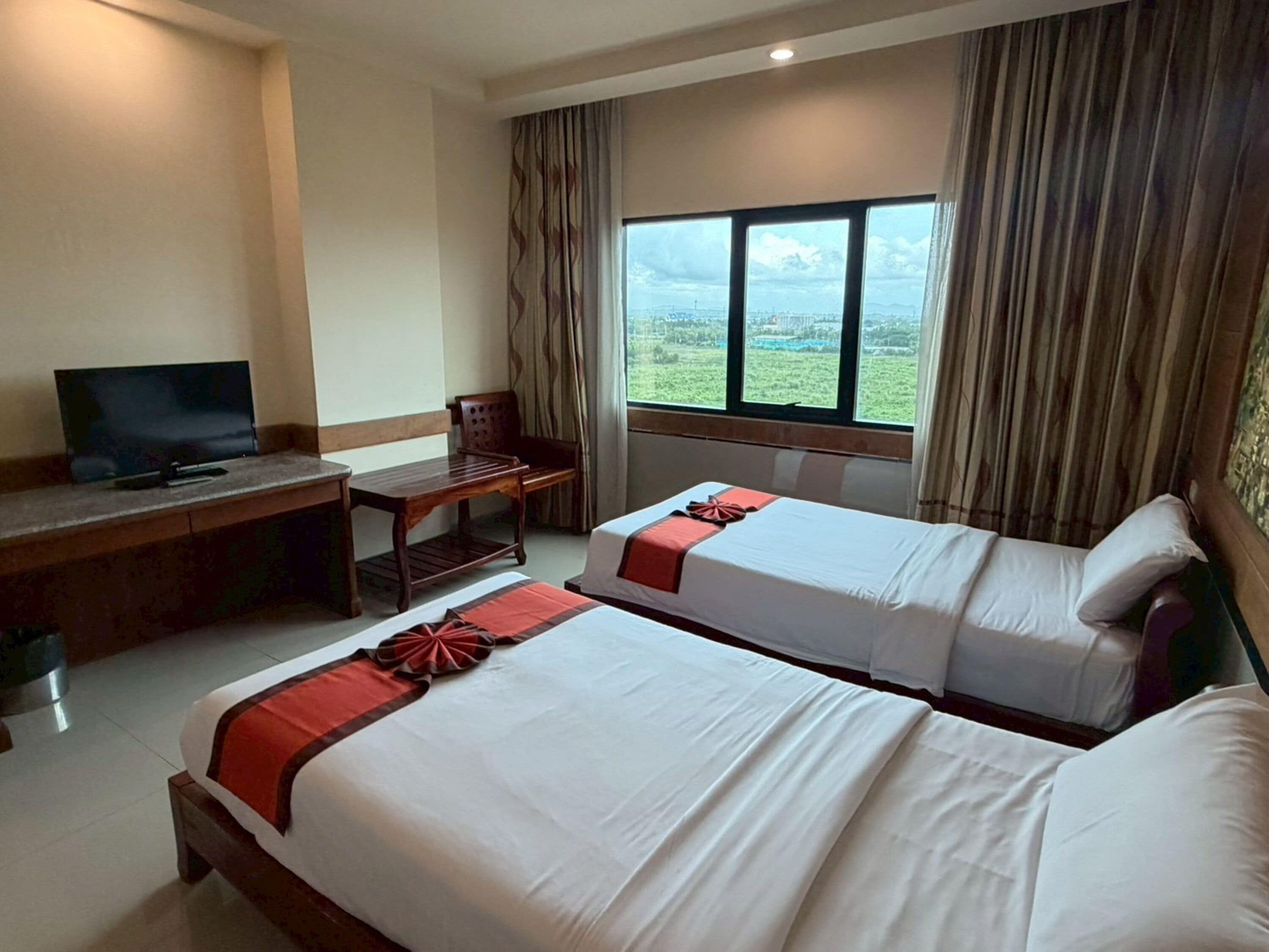 A hotel room with two beds, a desk with a television, and a window with curtains.