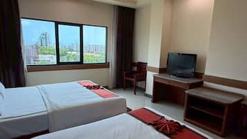 A hotel room with two beds, a desk with a television, and a view of a cityscape through large windows.