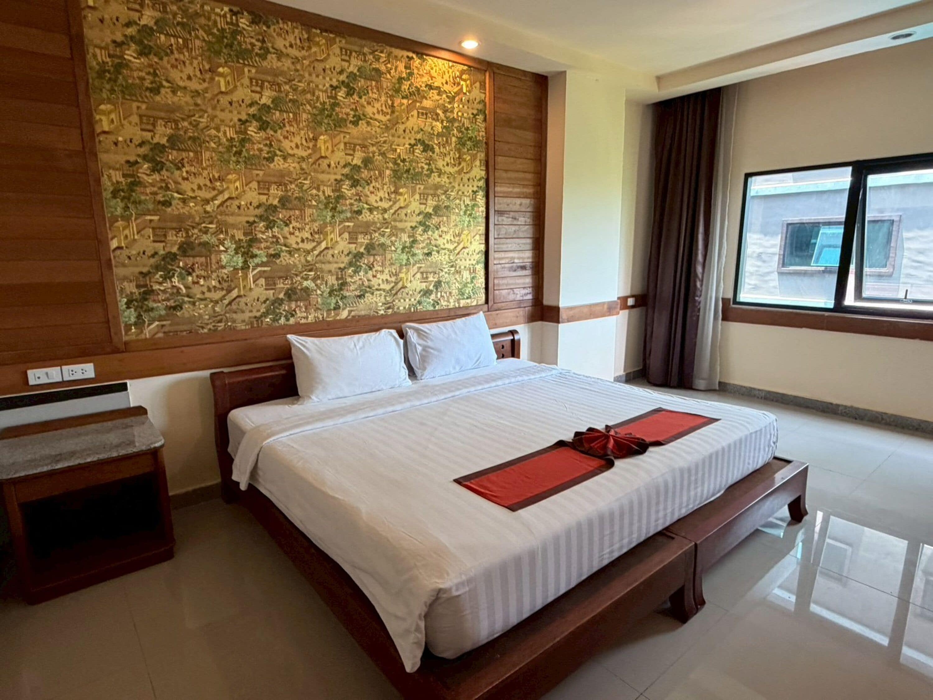 Habitación de hotel con una cama grande, cabecera de madera, un mural en la pared, una mesita de noche y una ventana con cortinas.