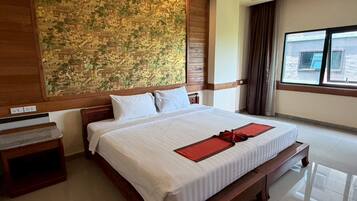 Habitación de hotel con una cama grande, cabecera de madera, un mural en la pared, una mesita de noche y una ventana con cortinas.