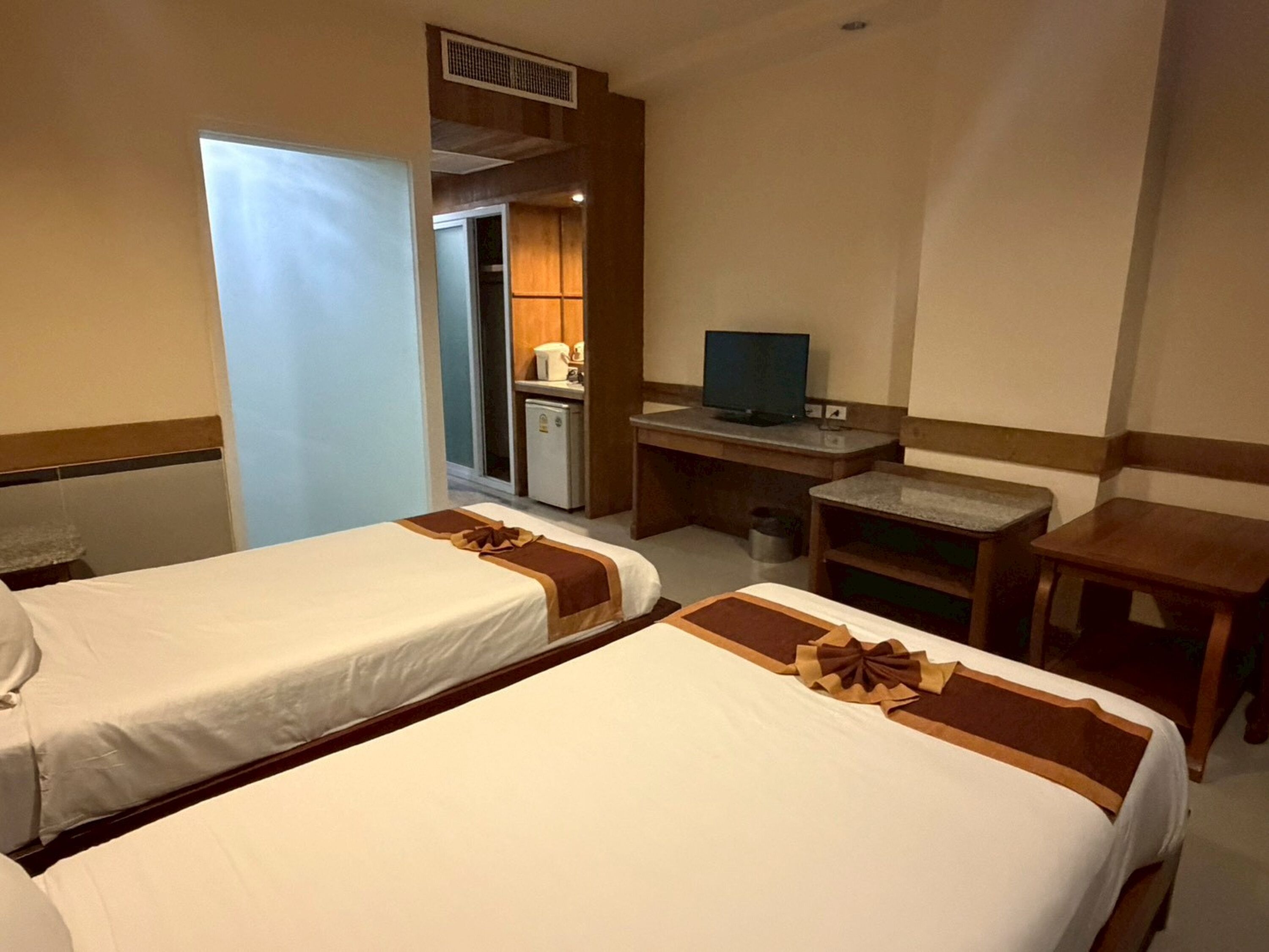 A hotel room with two beds, a desk, a television, and a kitchenette.