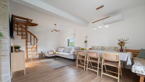 A spacious living area with a wooden staircase, a sofa, a dining table with chairs, and a TV mounted on the wall. - River House Val Gorski kotar (Pribanjci)