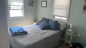 A bedroom with a bed, two nightstands, a wall clock, a framed certificate, and a standing fan.