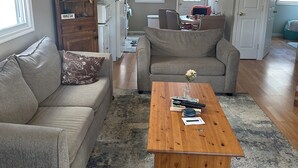 A living room with a wooden coffee table, two sofas, a bookshelf, and a kitchen area in the background.