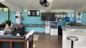 A modern hotel lobby with a sofa, a TV, a dartboard, and a reception desk.