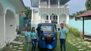 A house with a balcony, a blue auto-rickshaw, and a well-maintained lawn.
