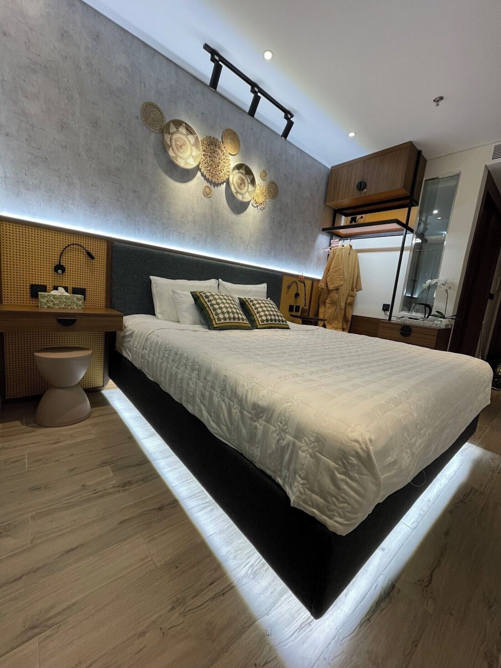 A modern bedroom with a large bed, a bedside table, a wall-mounted light fixture, and a wooden headboard.