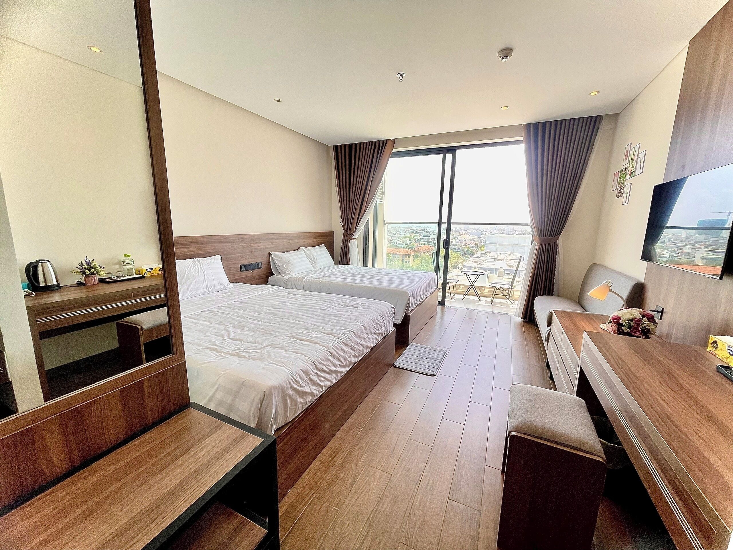 Une chambre d’hôtel avec deux lits, un bureau, une chaise, une télévision et un balcon donnant sur la ville.