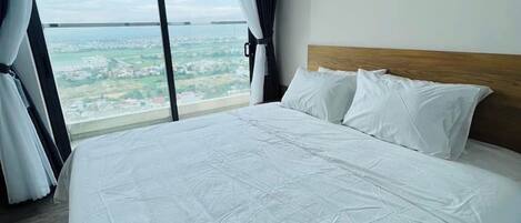 A hotel room with a large bed, a view of the city, and a painting on the wall.