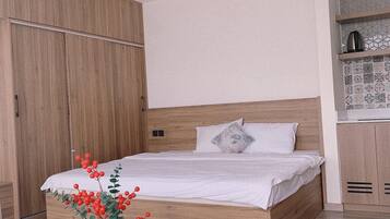 Ein modernes Schlafzimmer mit einem hölzernen Bett, weißer Bettwäsche, einem kleinen runden Tisch mit Teeservice und einer Zimmerpflanze.