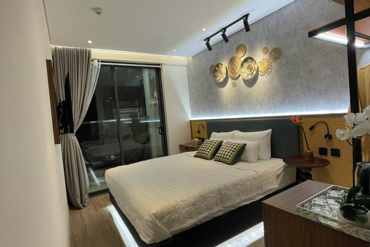 A modern bedroom with a large bed, a glass door leading to a balcony, and a wall-mounted light fixture.