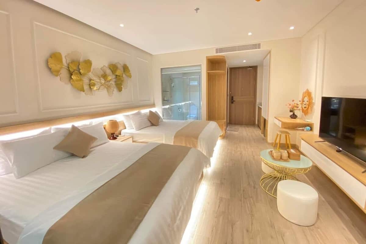 A modern hotel room with two beds, a TV, a small round table, and a decorative wall piece.