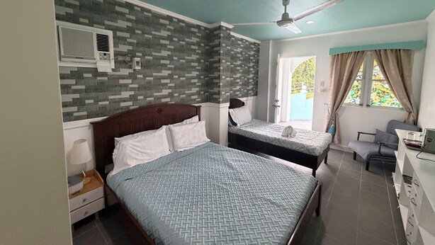 A hotel room with two beds, a ceiling fan, a window with curtains, and a small desk with a chair.