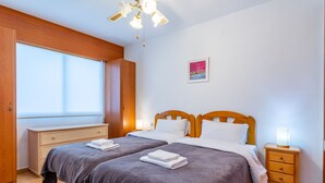 Une chambre double avec deux lits, une armoire en bois, une table de chevet avec une lampe et une fenêtre avec des stores.