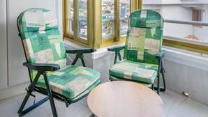 Un balcon avec deux chaises vertes et une petite table ronde, donnant sur un paysage urbain.