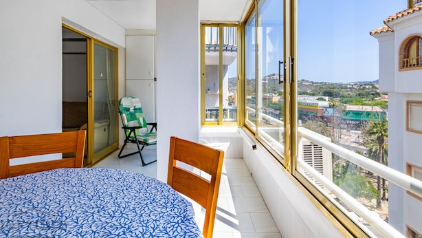 Un balcon avec une table et des chaises, une porte-fenêtre coulissante et une vue sur le paysage urbain.