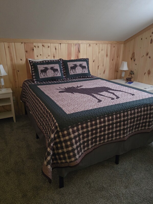 A bedroom with a bed, two pillows, a nightstand, and a lamp.