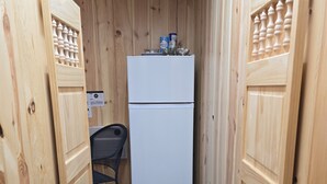Een smalle houten gang met een witte koelkast en een stoel.