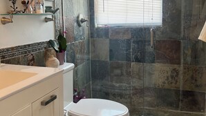 Un baño con inodoro blanco, cabina de ducha de vidrio y pared de azulejos.