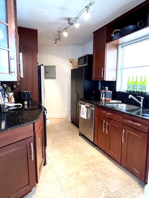A kitchen with wooden cabinets, a stainless steel refrigerator, a microwave, and a window with bottles.