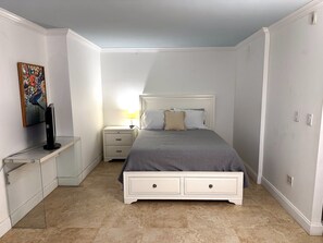 A bedroom with a bed, bedside table, lamp, and a painting on the wall.