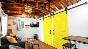 Una habitación con techo de madera, una puerta corredera, televisor, mesa y sofá.