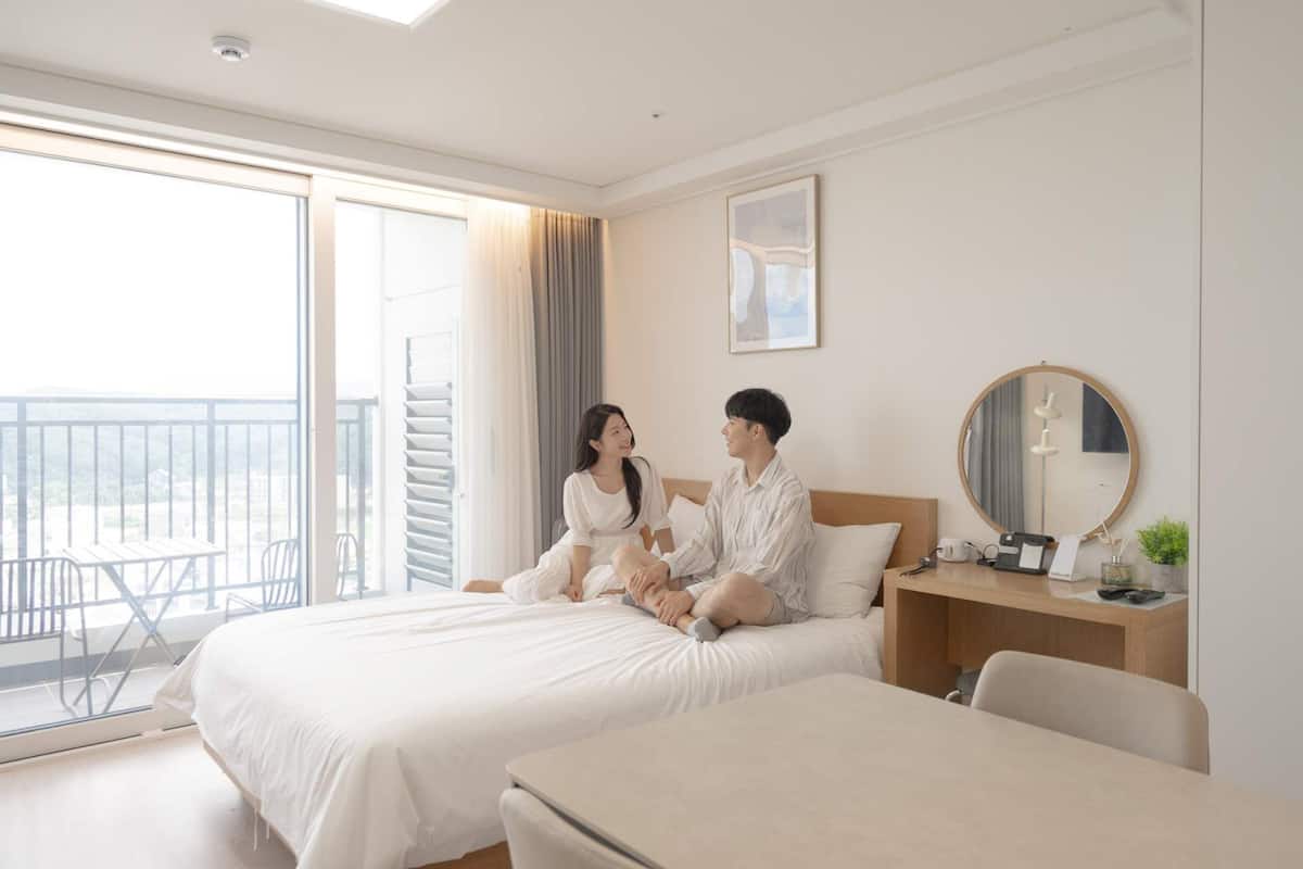A hotel room with two beds, a balcony, a desk with a mirror, and a painting on the wall.