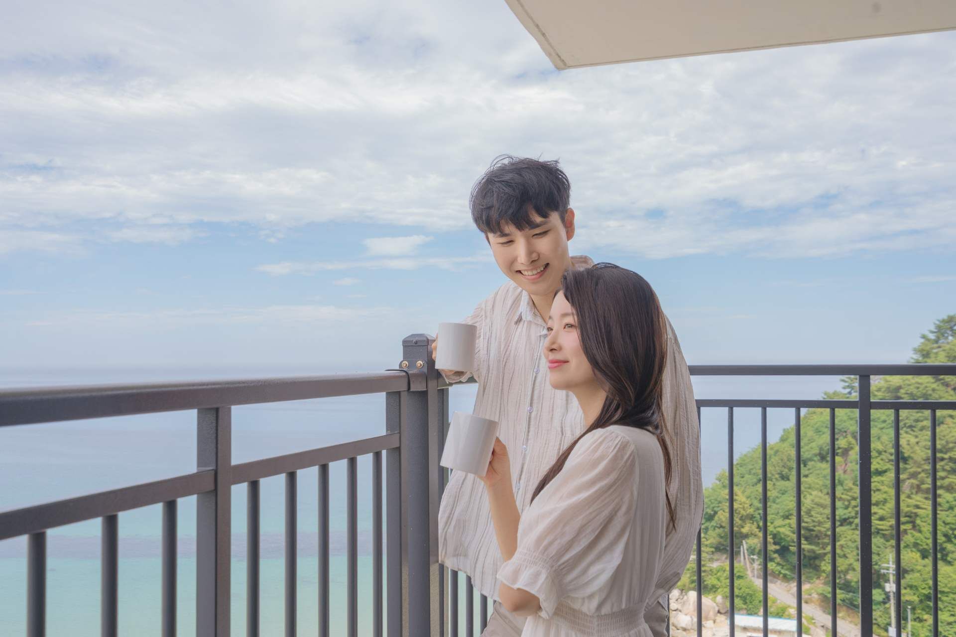 Una pareja en un balcón con vista al mar y vegetación.