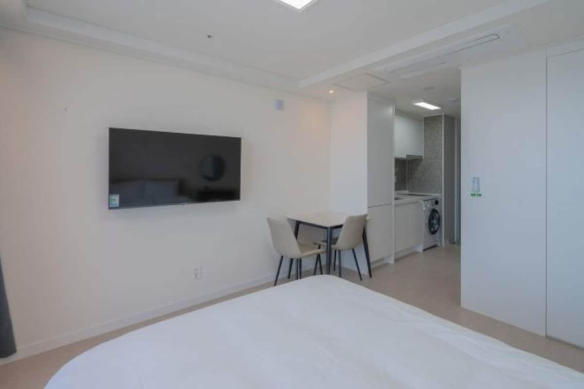 Habitación de hotel con una cama, una pequeña mesa con sillas, un televisor en la pared y una kitchenette al fondo.