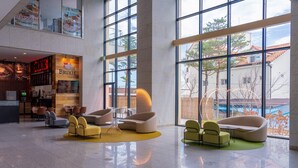 Un vestíbulo amplio con ventanas grandes, asientos modernos y un área de restaurante a la vista.