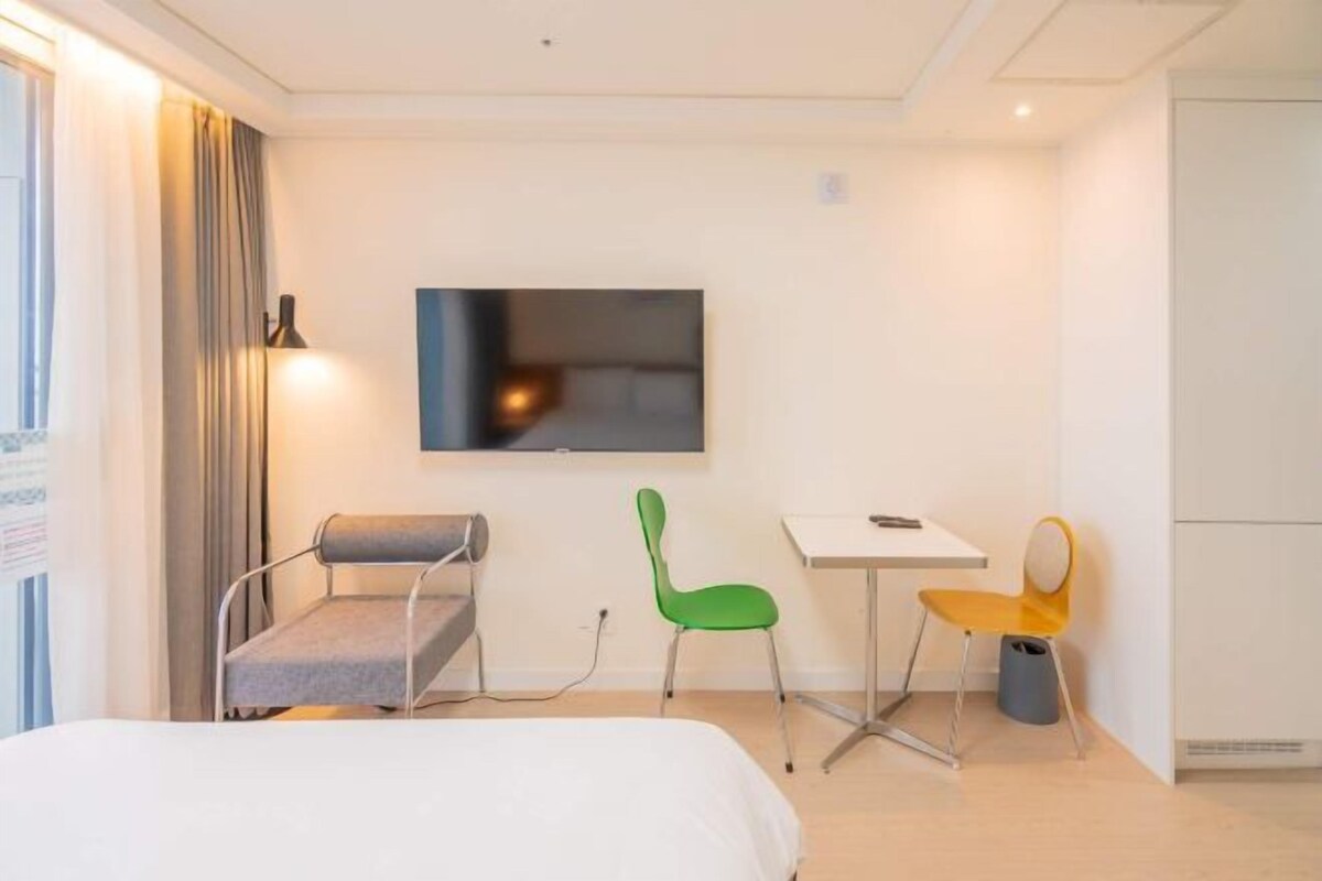 A hotel room with a bed, a desk, a chair, a TV, and a window with curtains.