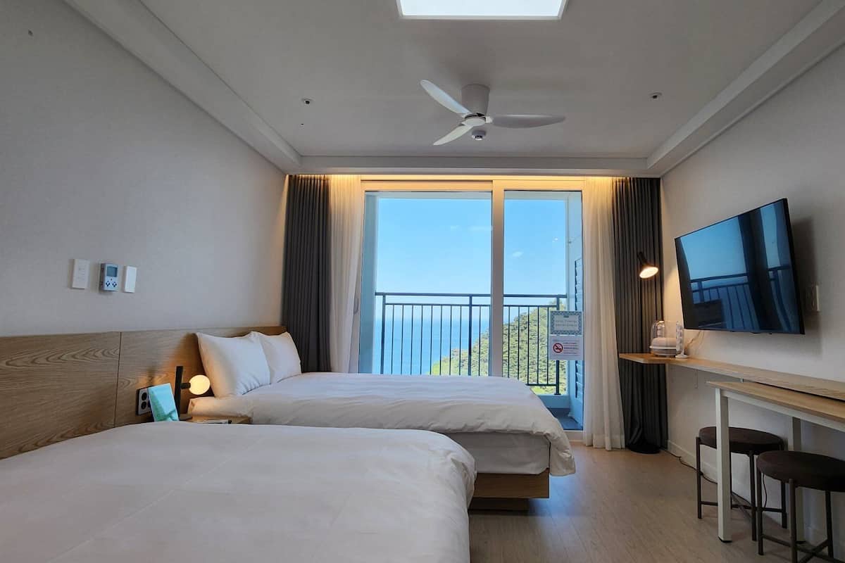 A hotel room with two beds, a TV, a desk with a chair, and a balcony with a view.