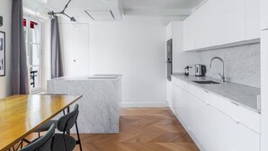 A modern kitchen with white cabinetry, a marble countertop, and a herringbone wood floor.