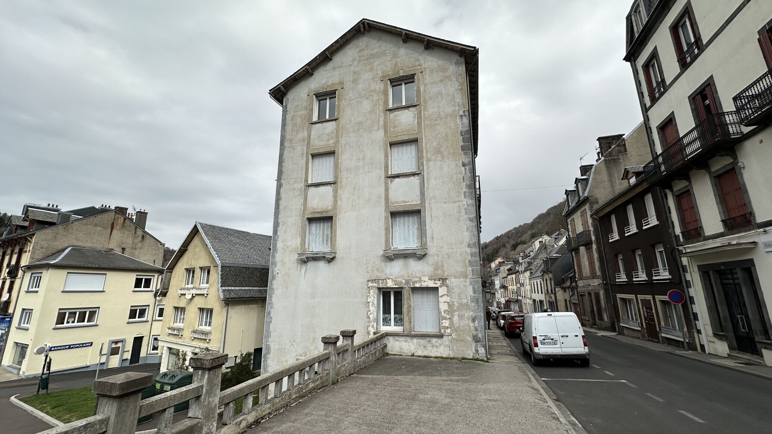 Une rue étroite bordée d’un grand immeuble rectangulaire doté de nombreuses fenêtres et d’une petite entrée.