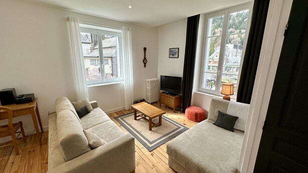A living room with a sofa, a coffee table, a TV, and a window with curtains.