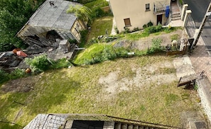 Un barrio residencial con césped, un edificio en ruinas con techo derrumbado, y un edificio moderno de dos pisos con balcón.