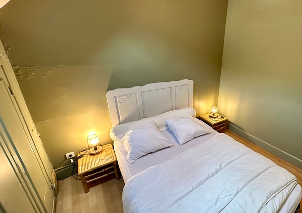 Una cama bien hecha con ropa de cama y almohadas blancas, dos lámparas de noche y una mesita de noche de madera.