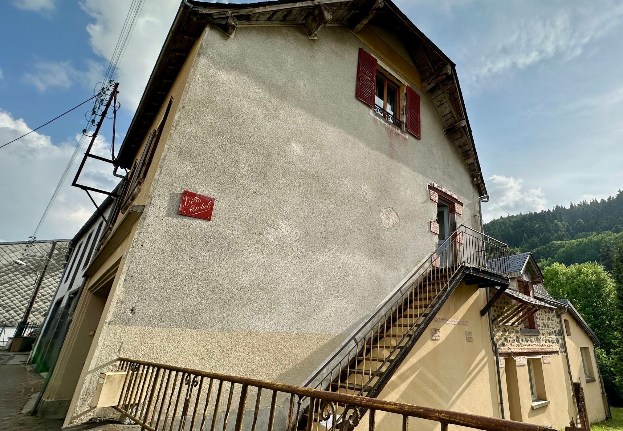 A building with a staircase leading to a balcony, a sign reading 'Villa Michel', and a clear sky.