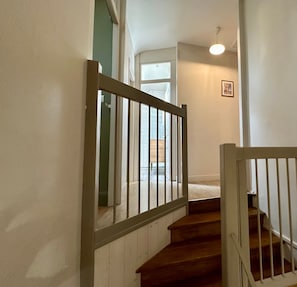 Una escalera con escalones de madera y barandillas blancas que conduce a una habitación con un ventanal y una lámpara en el techo.