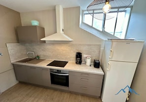 Cocina compacta con lavamanos, estufa y refrigerador, con ventanal sobre el lavamanos para luz natural.