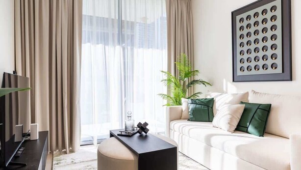 A modern living room with a sofa, a coffee table, a TV, and a large window with curtains.