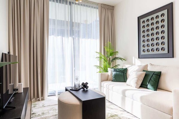 Una sala de estar moderna con sofá, mesa de centro, televisor y un amplio ventanal con cortinas.