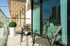 Un balcón con puerta de cristal, una planta en maceta, una mesita y una silla de mimbre.