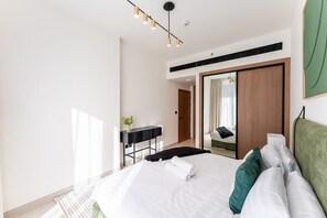 A modern hotel room with a large bed, a desk, a mirror, and a green headboard.